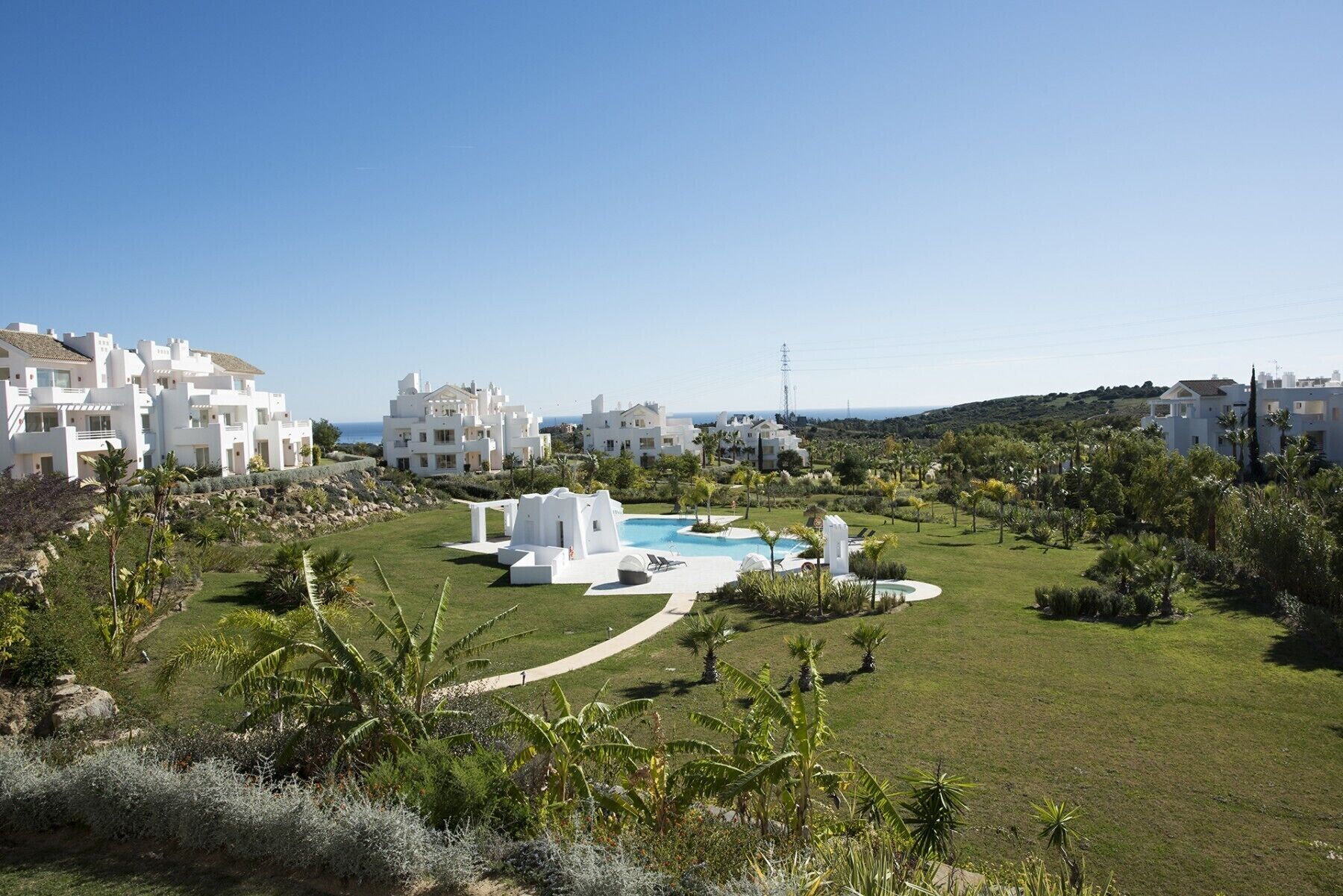 Un resort con edifici bianchi, una piscina e una vista limpida sul mare.