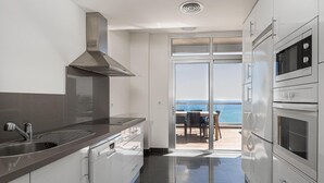 A modern kitchen with a stainless steel sink, a built-in oven, and a view of the sea through a glass door. - Punta Paloma Penthouse 2364 Sea View (Manilva)