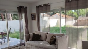 Un salon moderne avec un canapé, une table basse et une vue sur un jardin grâce à de grandes fenêtres.