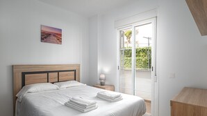 Ein Schlafzimmer mit einem hölzernen Kopfteil, einem Bett mit weißer Bettwäsche, einem Nachttisch mit Lampe und Blick ins Grüne durch eine Glastür.