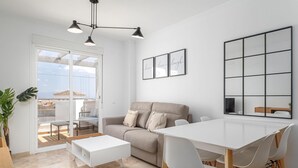 En moderne stue med sofa, spisebord og stole. Der er et stort vindue med udsigt over byen.