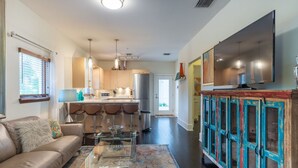 A modern living room with a sofa, coffee table, and a TV. There is a kitchen in the background with a refrigerator and a dining area. - Light, Bright and Full of Delight! 2 Blocks to Park Ave (Winter Park)