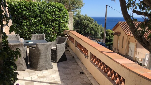 An outdoor patio with wicker furniture, a blue towel, and a table with a drink. - BEAUTIFUL 3-ROOM APARTMENT WITH SEA VIEW - LES ISSAMBRES (Roquebrune-sur-Argens)