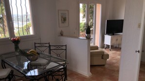 A dining area with a glass table, chairs, and a bowl of fruit. There is a sofa and a television in the background. - BEAUTIFUL 3-ROOM APARTMENT WITH SEA VIEW - LES ISSAMBRES (Roquebrune-sur-Argens)