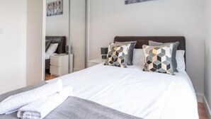 A neatly made bed with a white duvet and patterned pillows, a bedside table with a lamp, and a mirror on the wall. - Impeccable 2-bed Apartment in Reading (Reading)
