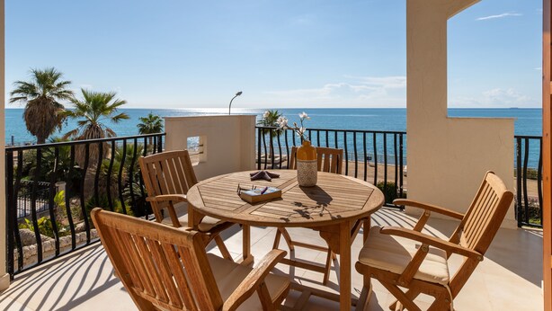 A wooden table and chairs on a balcony with a view of the sea. - Apartment (Marina di Ragusa)
