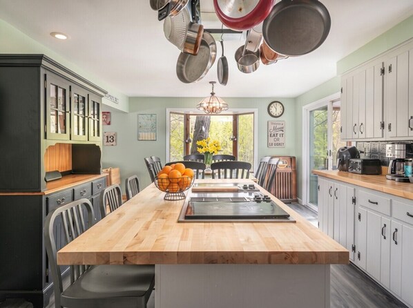 A kitchen with a central island, a dining area with chairs, and a view through the window.