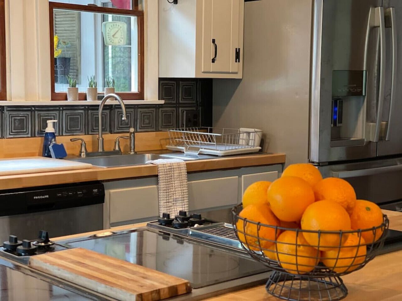 Une cuisine moderne équipée d’une cuisinière à gaz, d’appareils électroménagers en acier inoxydable et d’un saladier rempli d’oranges posé sur le plan de travail.