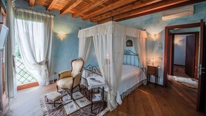 Ein Schlafzimmer mit Himmelbett, Holzboden und Blick ins Freie durch ein Fenster.
