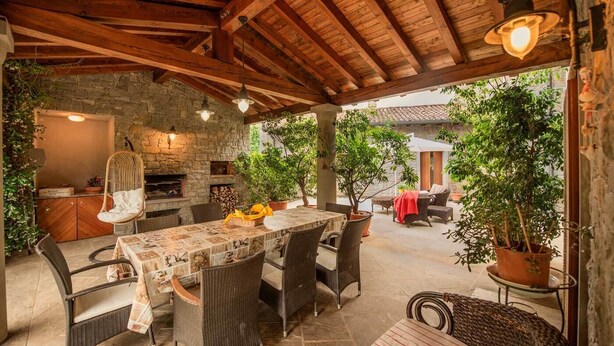 Eine Terrasse im Freien mit Kamin aus Stein, Korbmöbeln und Topfpflanzen.