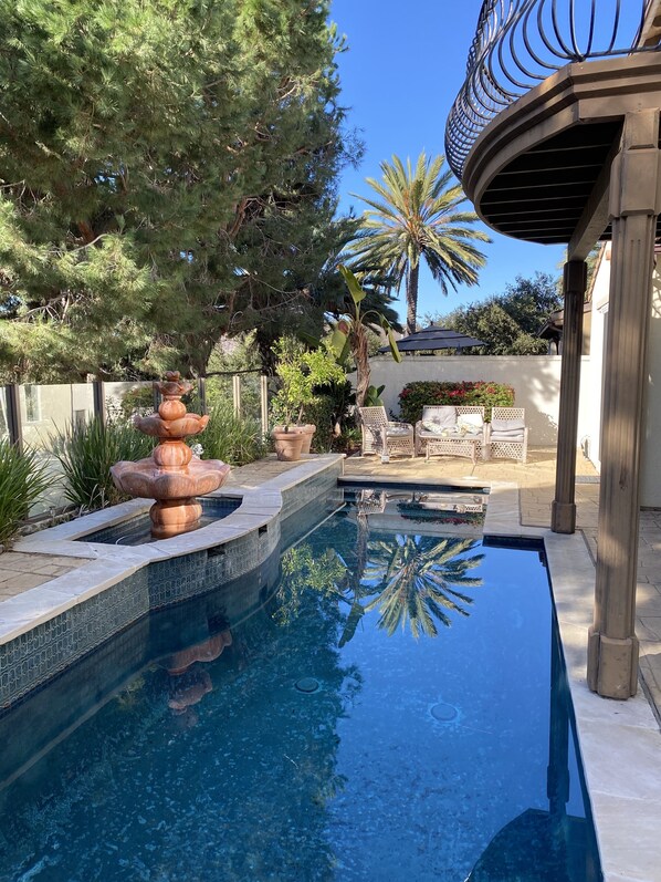 Relax by the serene pool surrounded by lush greenery and a tiered water feature.