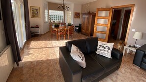 A spacious living area with a black leather sofa, a dining table with chairs, a chandelier, and a large wooden cabinet. - Weekly rental, villa Lloret de Mar with private pool, quiet area (Lloret de Mar)