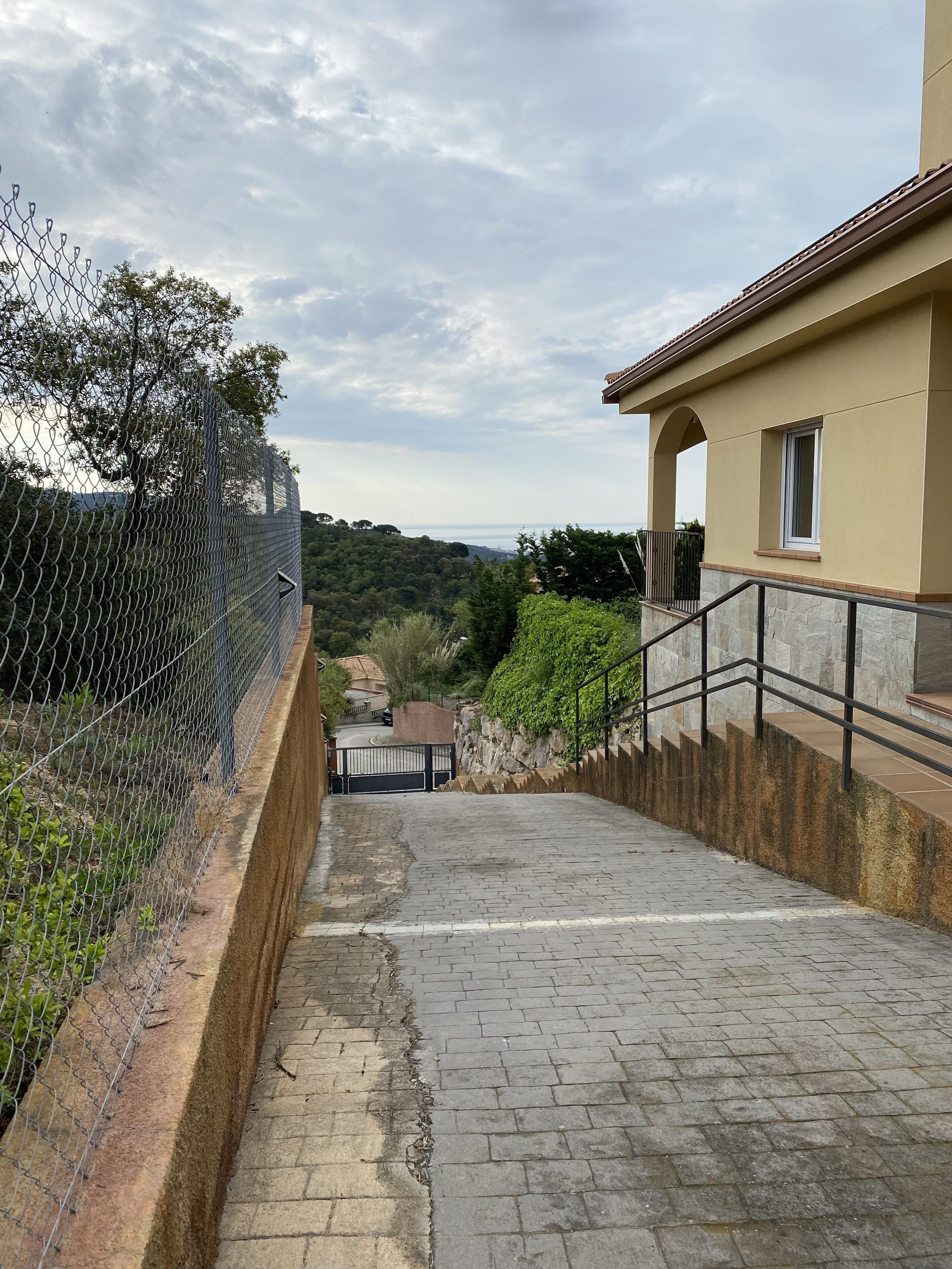 Un chemin pavé mène à un bâtiment doté d’un mur en pierre et d’une clôture en métal.