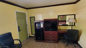 A room with a ceiling fan, a desk with a computer, a chair, and a microwave. - Vanguard Motel (Navasota)