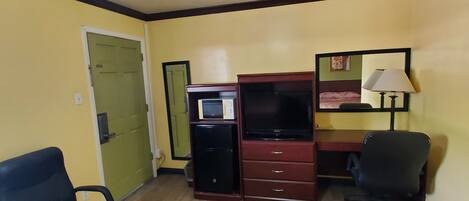 A room with a ceiling fan, a desk with a computer, a chair, and a microwave.