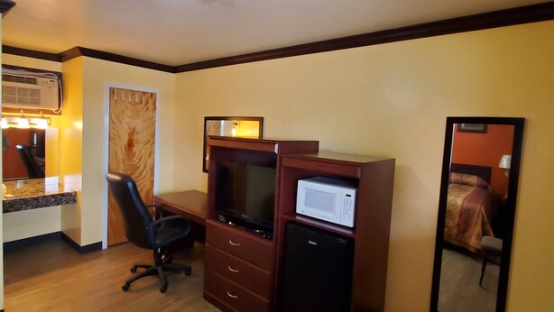 A hotel room with a wooden desk, a chair, a small refrigerator, a microwave, and a large mirror. - Vanguard Motel (Navasota)