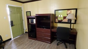 A hotel room with a wooden desk, a chair, a television, a microwave, and a green door. - Vanguard Motel (Navasota)