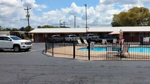 A fenced outdoor swimming pool area with a building in the background. - Vanguard Motel (Navasota)