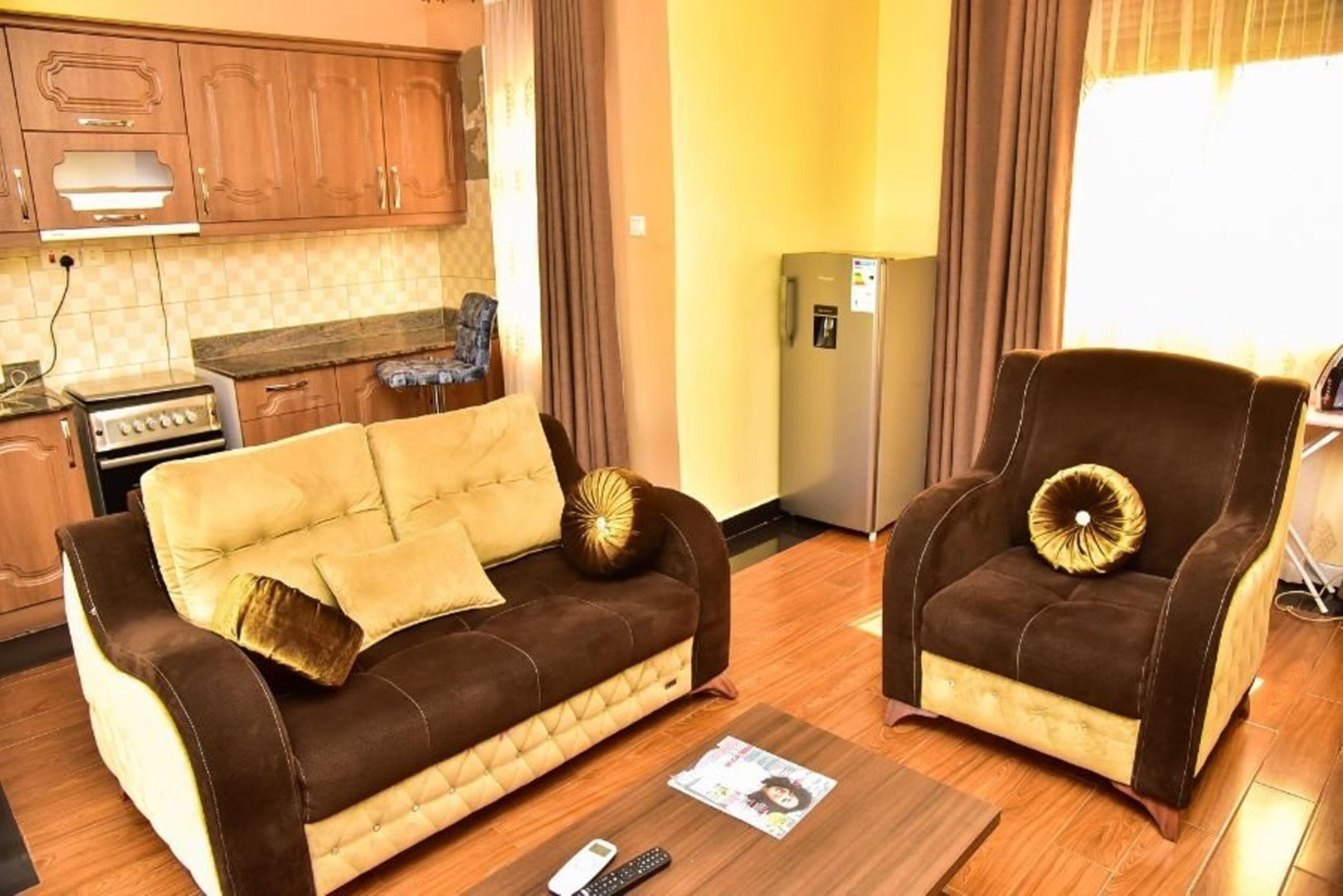 Una sala de estar con sofá y sillón, un área de cocina con armarios y estufa, y un refrigerador.