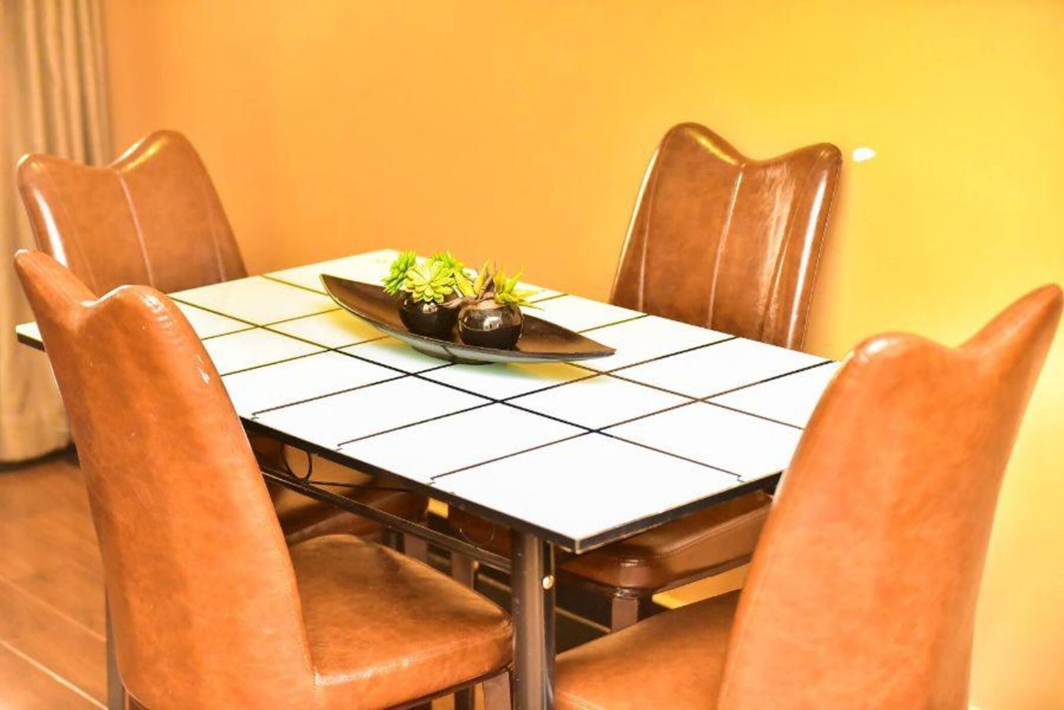 A dining table with a tiled top, surrounded by four brown leather chairs.