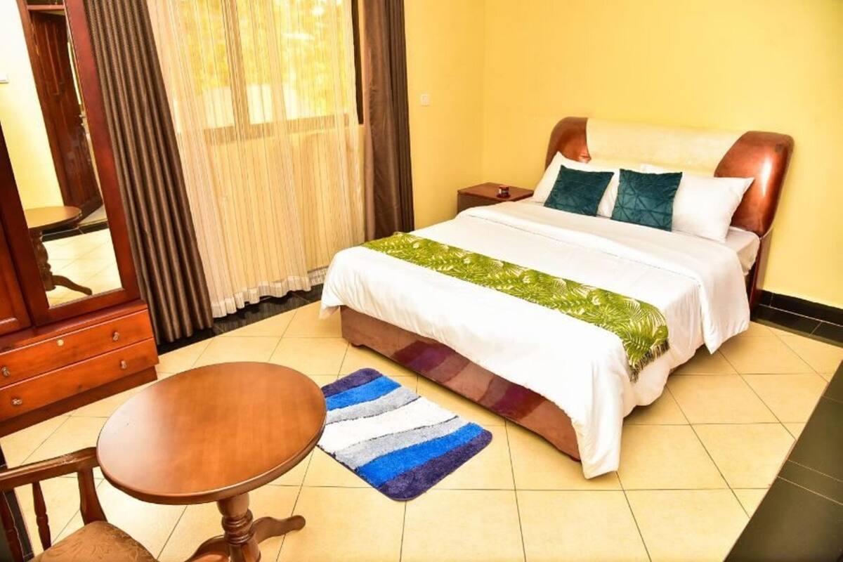 Una habitación de hotel con una cama, una mesita de noche de madera, una pequeña mesa y una silla.