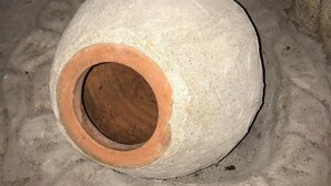 Une grande structure circulaire en béton, dotée d’un espace central creux, qui pourrait être un puits ou un élément décoratif, située dans une pièce dont le sol est en béton et le plafond, en poutres de bois.