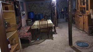 Une pièce faiblement éclairée, avec une table et des chaises, des étagères remplies de divers objets et un mur en pierre.