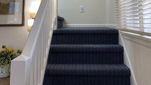A staircase with patterned carpet, a framed painting, and a potted plant. - Eagles Nest Cottage in Egg Harbor, Door County, WI (Egg Harbor)