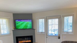A living room with a fireplace, a television, and two ottomans. - Eagles Nest Cottage in Egg Harbor, Door County, WI (Egg Harbor)
