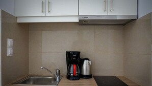 A compact kitchen with a sink, a coffee maker, a kettle, and a black induction cooktop.