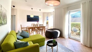 Un salon moderne avec un canapé vert, une table à manger et une grande fenêtre agrémentée de rideaux.
