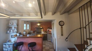 Eine Küche mit Kochinsel, Barhocker, Esstisch und einer Treppe mit Geländer.
