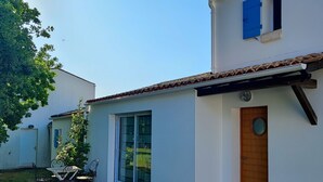 Ein modernes, zweistöckiges Haus mit weißer Fassade, einer Holztür und einem blauen Fensterladen.
