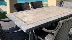 Patio esterno con tavolo e sedie, piscina e zona coperta con pergolato.