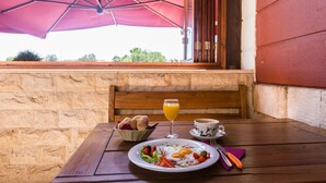 Una mesa de madera con alimentos para el desayuno, como huevos, verduras y tostadas, bajo un paraguas rosa.