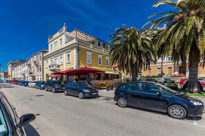A street lined with parked cars and a row of buildings with balconies and a red awning. - B&B Giardin (Zadar)