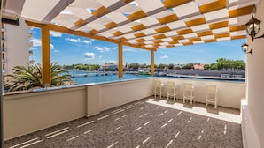 Un espacio al aire libre techado con suelo estampado, vista a la piscina y sillas blancas.