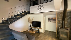 A modern living room with a staircase, a fireplace, a flat-screen TV, and a decorative wall piece.