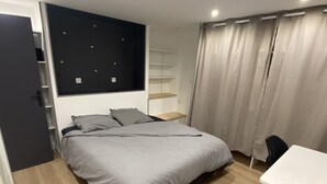A bedroom with a bed, a desk, and a shelving unit.