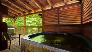 Eine Holzterrasse mit Whirlpool, Holzgeländern und Blick ins Grüne.