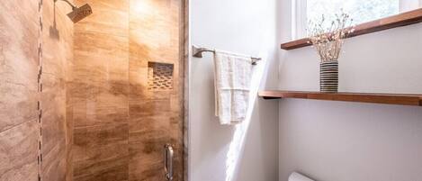 A modern bathroom with a shower, a toilet, and a window.