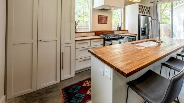 Una cucina moderna con mobili bianchi, un piano di lavoro in legno e un frigorifero in acciaio inossidabile.