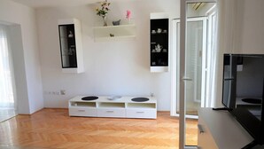 Un salon moderne avec un plancher en bois, un meuble de rangement blanc et un support de télévision noir.