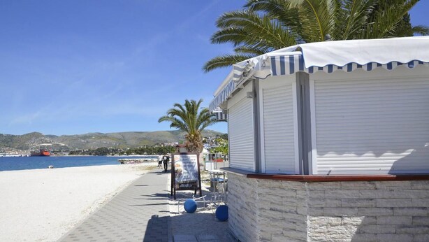 Un hôtel en bord de mer, avec une façade blanche, un revêtement en pierre et un espace extérieur abrité avec des sièges.