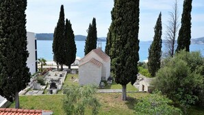 Un cimetière avec une petite chapelle, entouré de grands cyprès, qui surplombe une étendue d’eau.