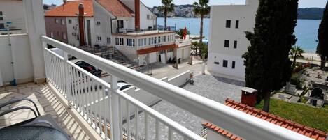 A balcony with a view of a coastal town, featuring buildings with red-tiled roofs, a clear sky, and a calm sea.