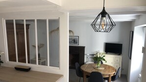 Ein Essbereich mit Holztisch und Stühlen, einer Hängeleuchte sowie einem Fernseher auf einem Schrank.