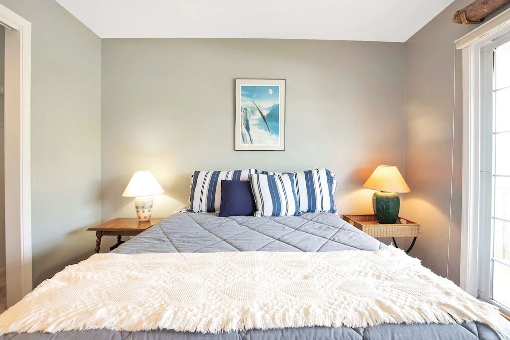 Une chambre à coucher avec un lit, deux tables de chevet, un tableau accroché au mur et une fenêtre.