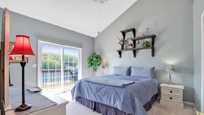 A bedroom with a bed, bedside tables, a red lamp, a plant, and a view through a sliding door. - Lakefront Family Retreat | Sleeps 10+ | Pet-Friendly | Swim & Fish Off the Dock (Sunrise Beach)