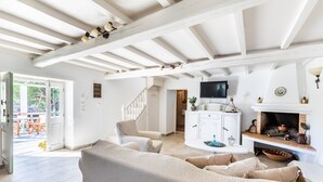 A spacious living room with a high ceiling, a fireplace, a television, and a staircase leading to another level.
